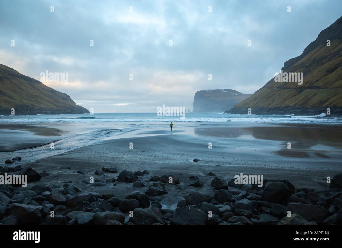 A surfer on the sandy beach of Tjørnuvík walking alone towards the ocean. Faroe Islands Stock Photo