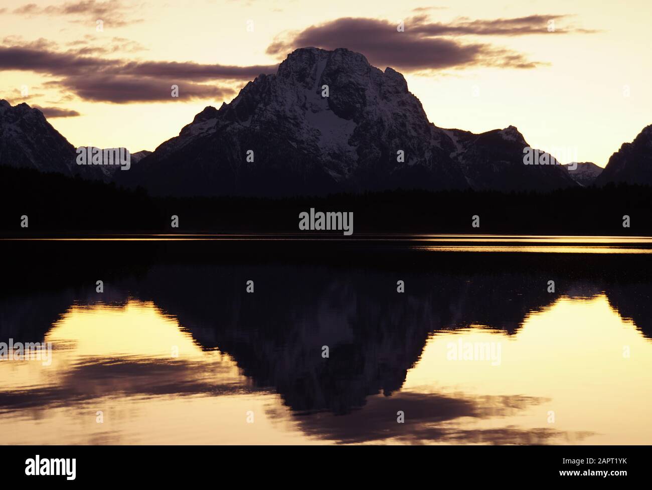 The still lake perfectly reflects the mountain in the background in the waning light after sunset. Stock Photo