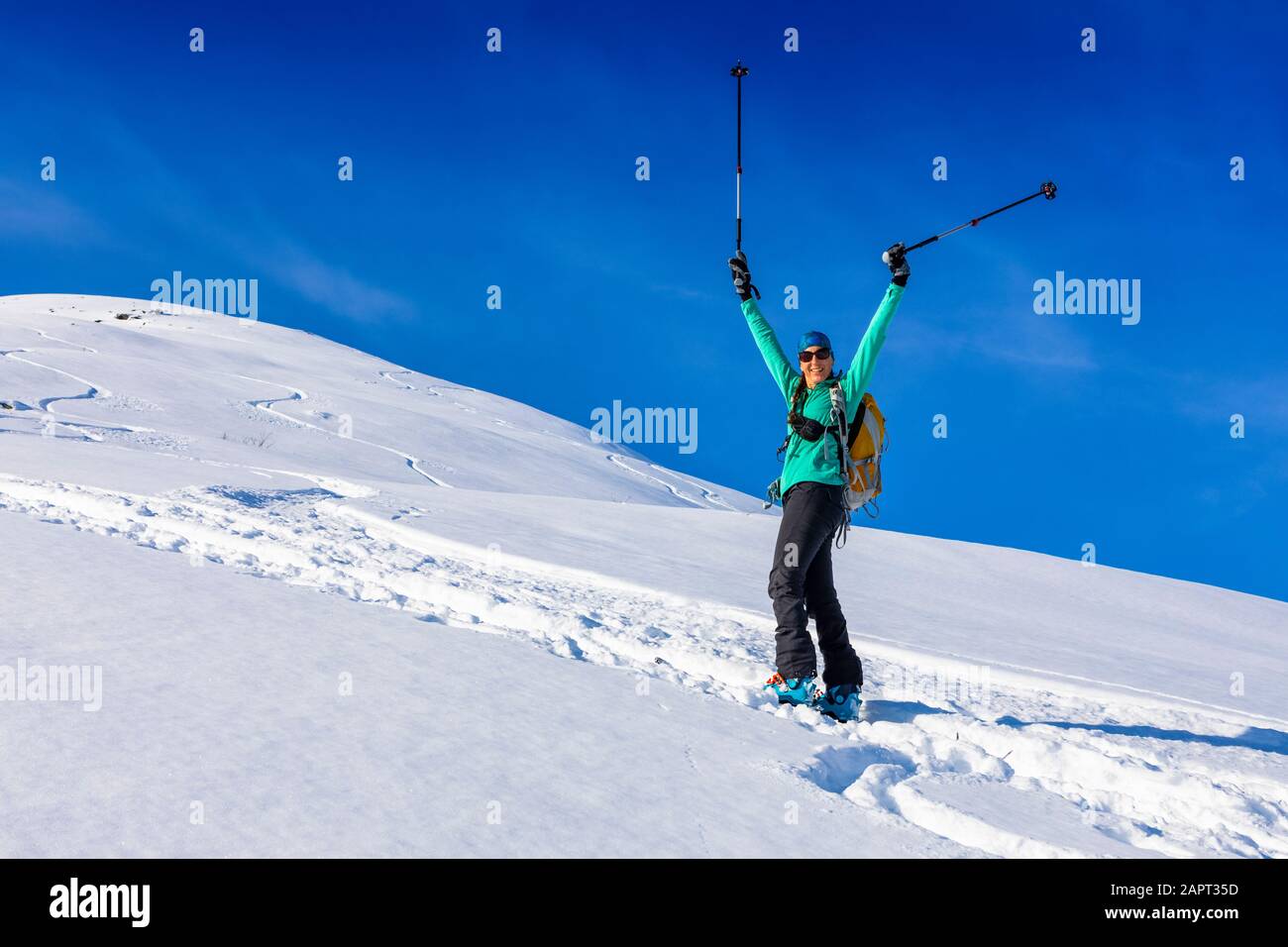 Woman backcountry skiing, celebrating a beautiful day with her poles in the air, climbing up mountain in skin track, on AT skis and skins in Hatche... Stock Photo