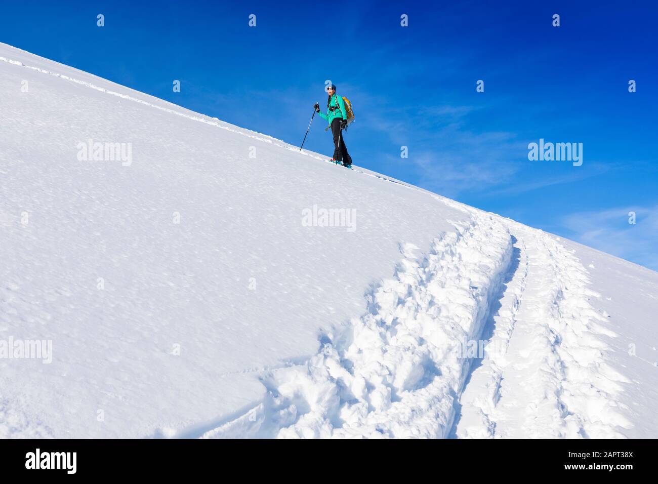 Woman backcountry skiing, climbing up mountain in skin track, on AT