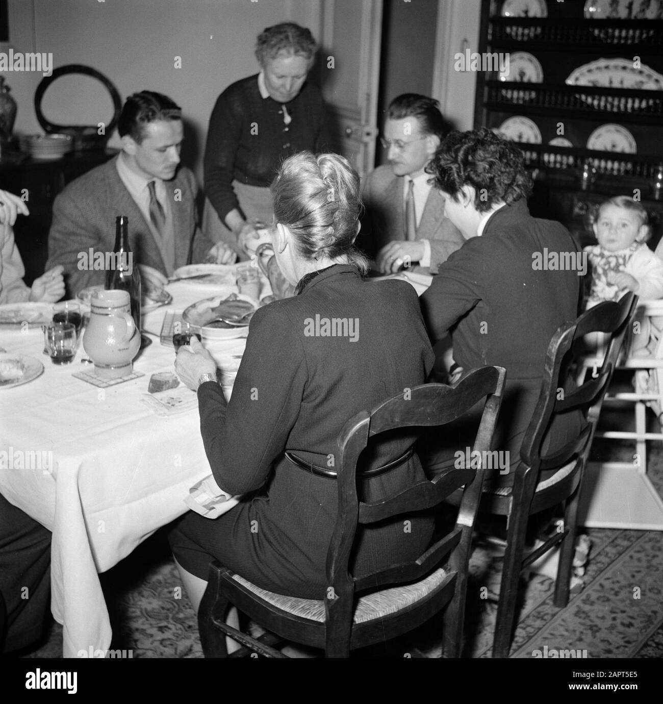 Residents of an apartment building in Paris  Family with guests at the meal Date: 1950 Location: France, Paris Keywords: families, bottles, meals Stock Photo