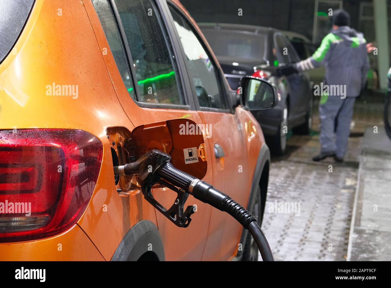 Car fill with diesel at petrol station. Pumping diesel fuel in orange car at gas station in evening. Stock Photo