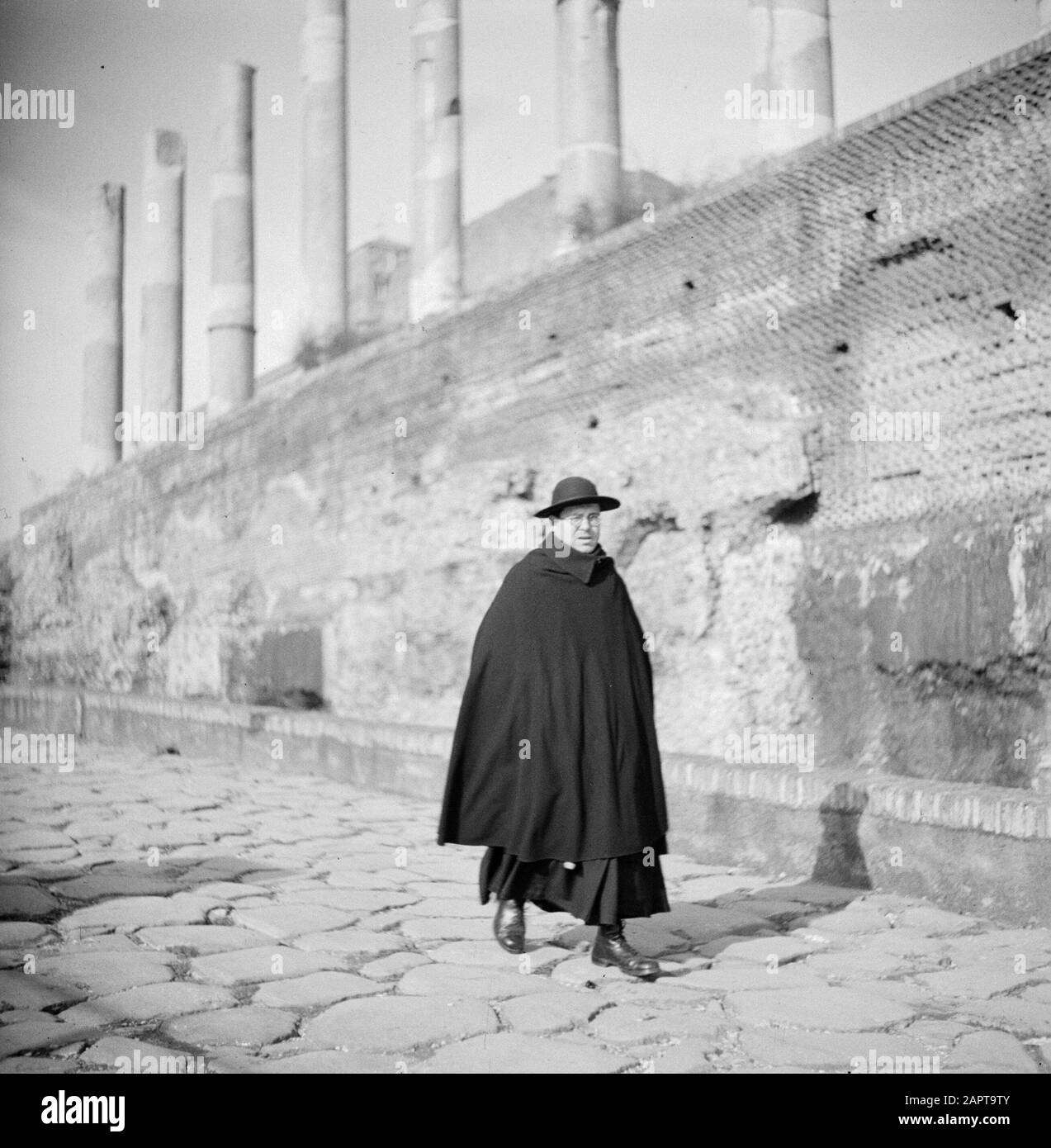 Rome: Visit to the city  Spiritual in a street near the Roman Forum Date: December 1937 Location: Italy, Rome Keywords: archeology, architecture, clergy, headcovers, Catholicism, pillars, ruins, street statues, uniforms Stock Photo