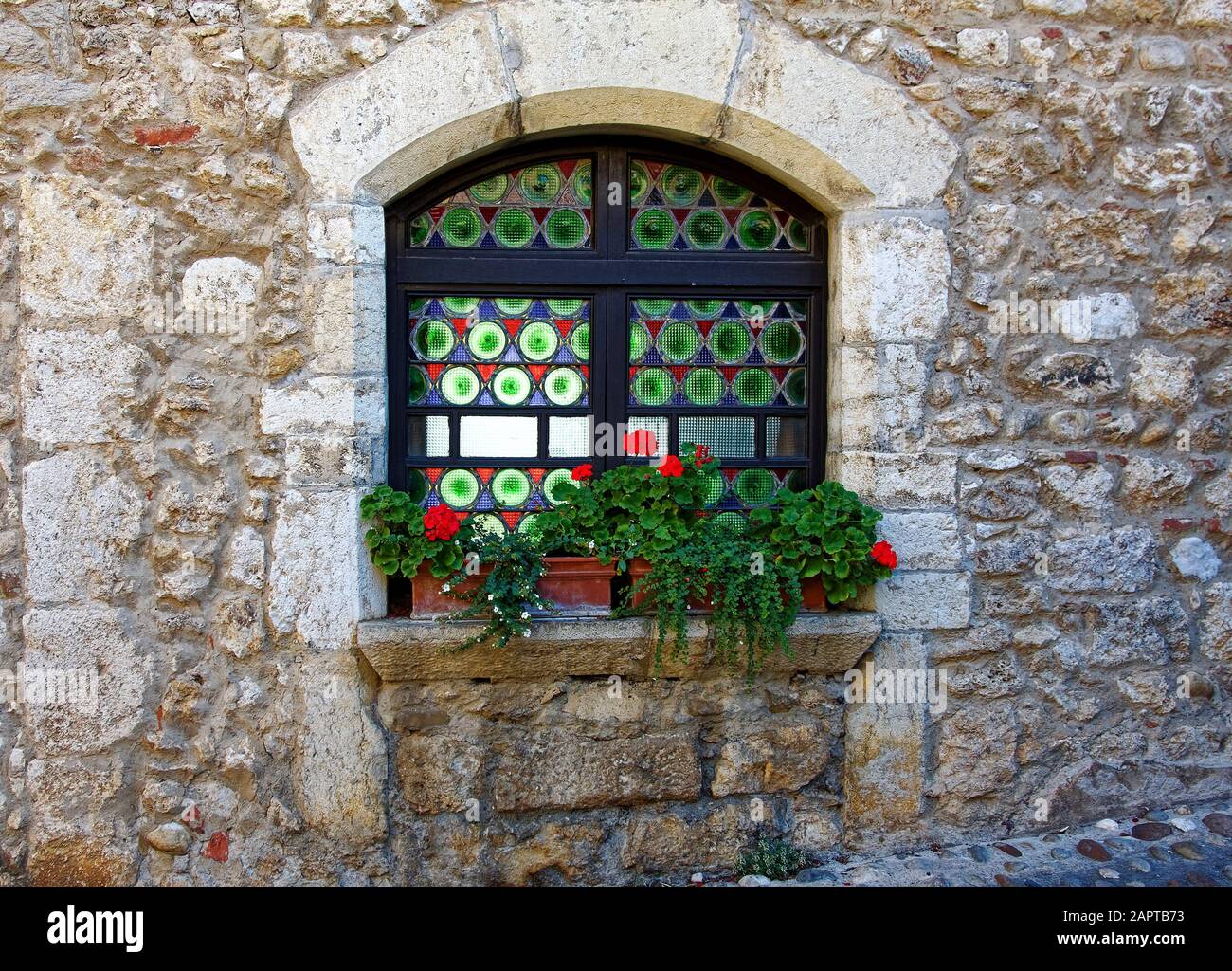 colorful glass window, arched, old stone building, windowsill, potted flowers, contrasting textures, Perouges, France, summer, horizontal Stock Photo