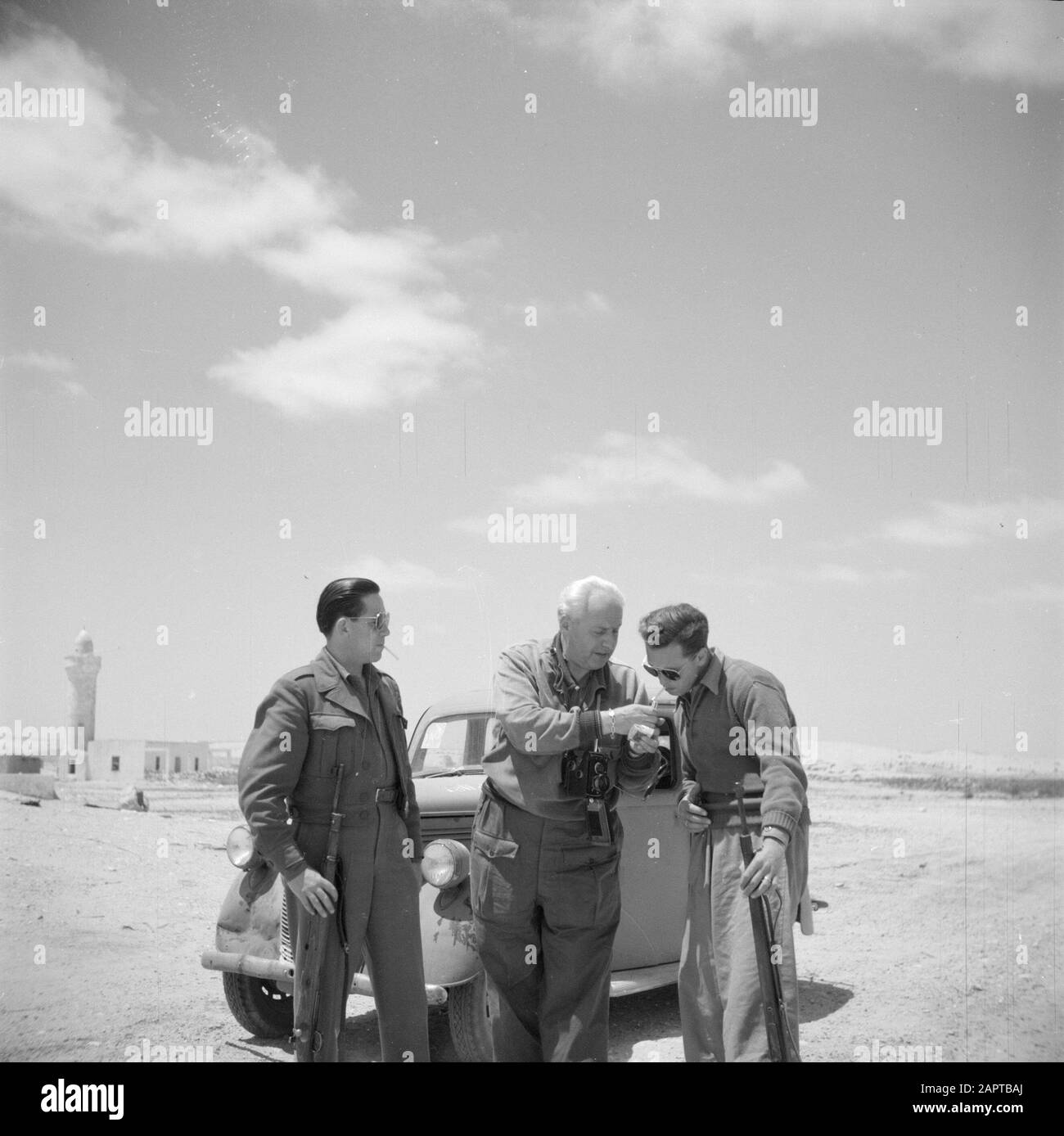 Israel 1948-1949: Negevdesert, travel company William van de Poll  Armed men standing in front of a car in the Negev Desert; in the middle photographer William of the Poll Annotation: The two men at both sides supposedly belonged to the travelling company of photographer Willem van de Poll Date: 1948 Location: Israel, Negev Keywords: cars, photographers, men, smoking, firearms, deserts Personal name: Poll, William of the Stock Photo