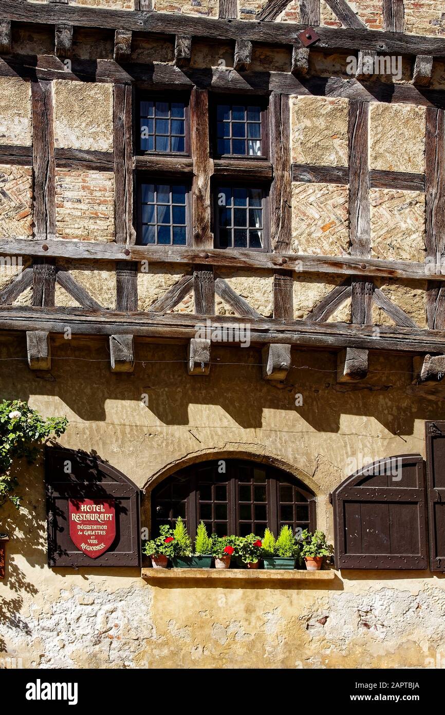 old half-timbered building, brick, stucco, wood, multiple windows, potted plants, hotel restaurant, Perouges, France, summer, vertical Stock Photo