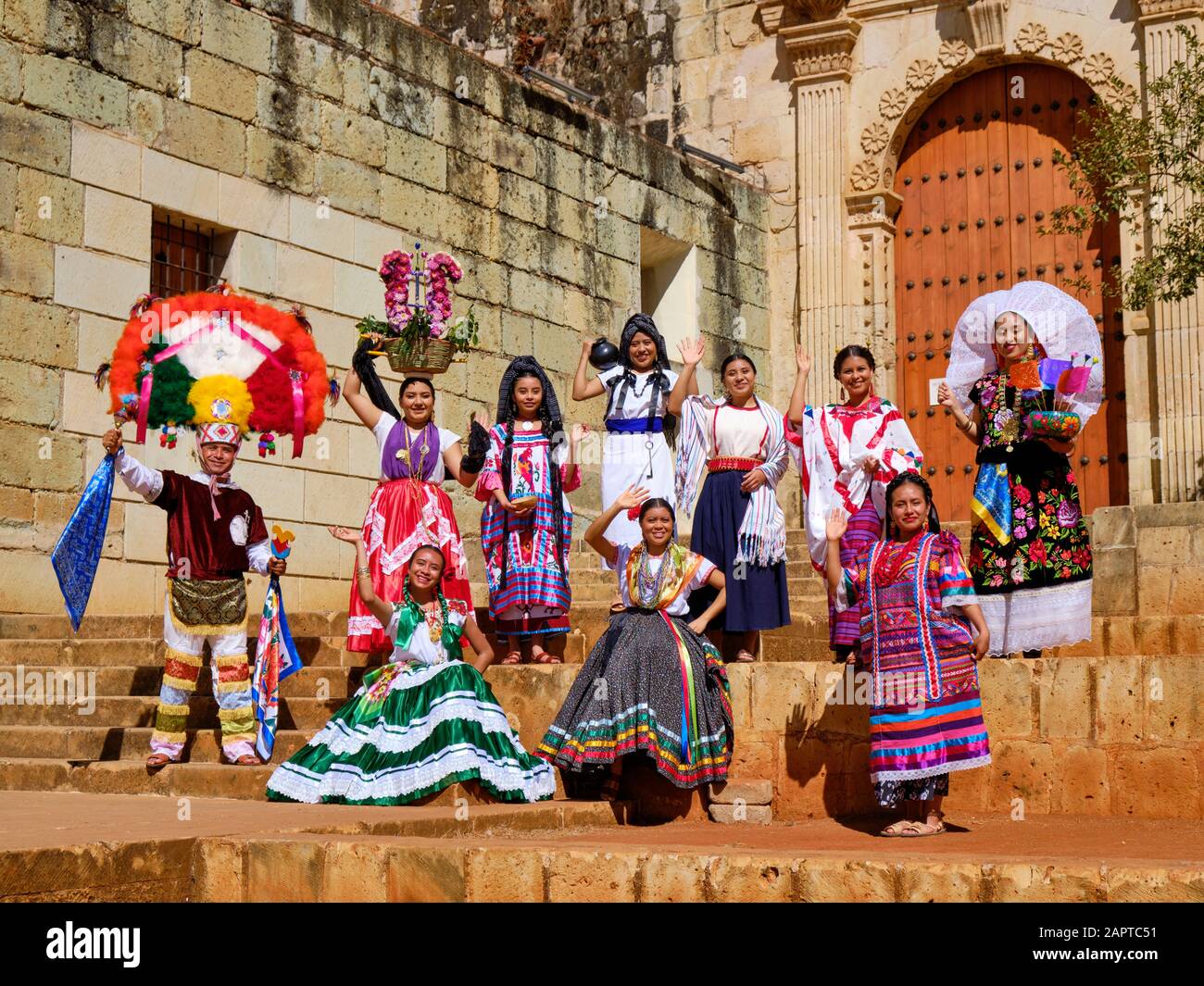 Group of people in traditional Mexican clothing posing and waving in midday sun at door of large church Stock Photo