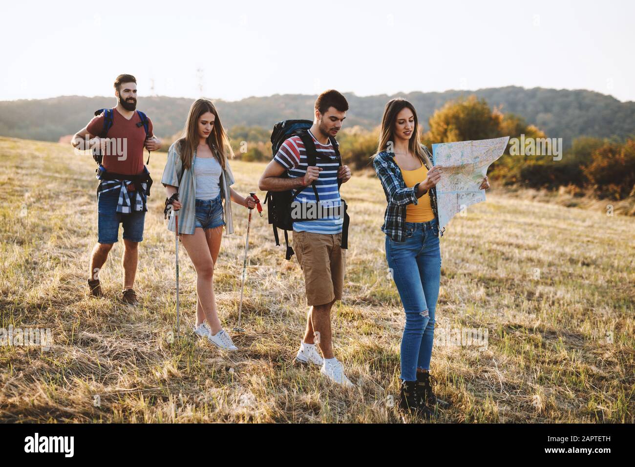adventure, travel, tourism, hike and people concept - group of smiling friends walking with backpacks in nature Stock Photo