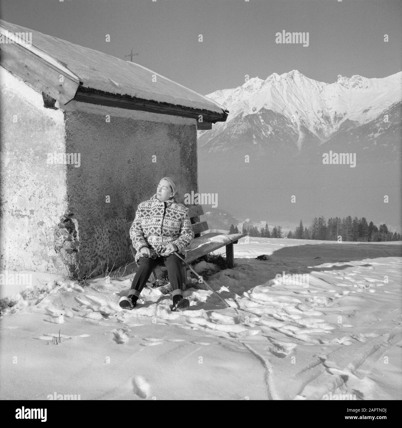 Winter in Tirol  Hilde Eschen on a bench at the Lemmenhof Chapel in the snow with in the background the Karwendel Mountains Date: January 1960 Location: Austria, Sistrans, Tyrol Keywords: mountains, chapels, landscapes, snow, holiday, winter Personal name: Echen, Hilde Stock Photo