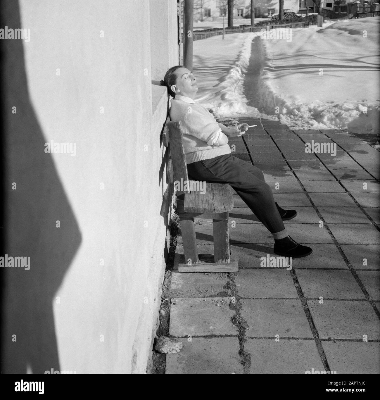 Winter in Tirol  Hilde Eschen sits sunbathing on a bench by a house Date: January 1960 Location: Austria, Sistrans, Tyrol Keywords: villages, snow, holiday, winter, homes Personal name: Eschen, Hilde Stock Photo
