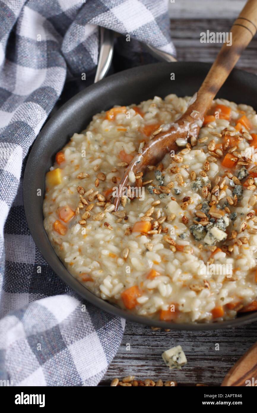 Butternut squash risotto with blue cheese and sunflower seeds with wood spoon, on rustic background with blue and white checkered towel Stock Photo