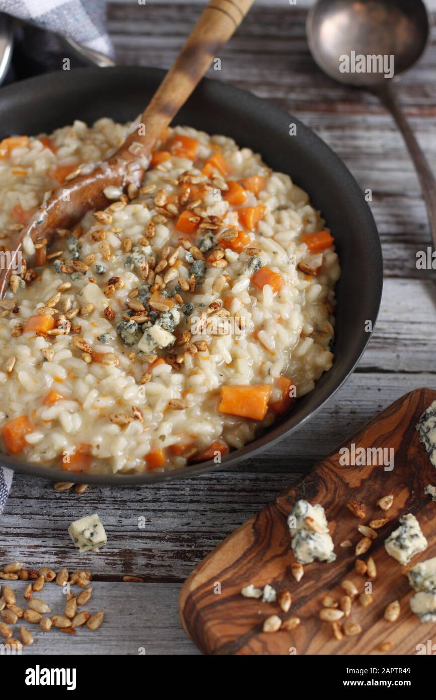 Butternut squash risotto with blue cheese and sunflower seeds, on rustic background with board, cheese and laddle Stock Photo
