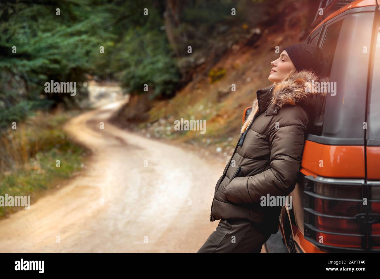 Enjoying mountainous silence, beautiful woman leaned on a car and enjoys nature with closed eyes, off-road car travel, active weekend, happy life Stock Photo