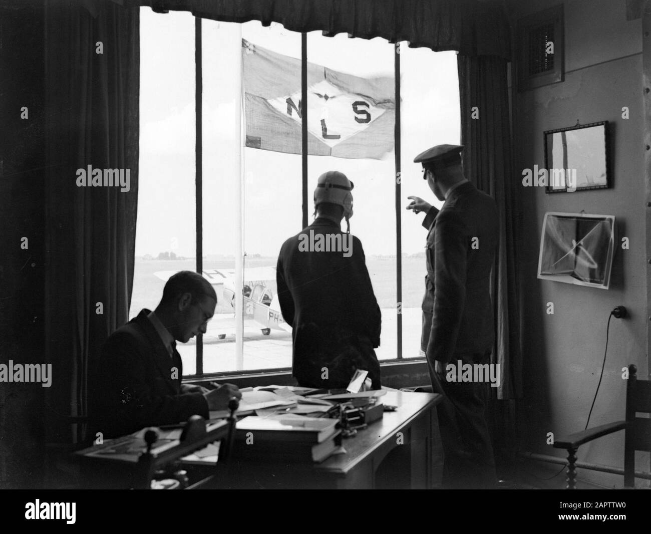 National Aviation School Holland  In the office of the National Aviation School Holland. The instructor assigns and outside taxiet a Koolhoven FK 46 biplane Date: July 1935 Location: Amsterdam, Noord-Holland Keywords: offices, pilots, flight training, aircraft Stock Photo
