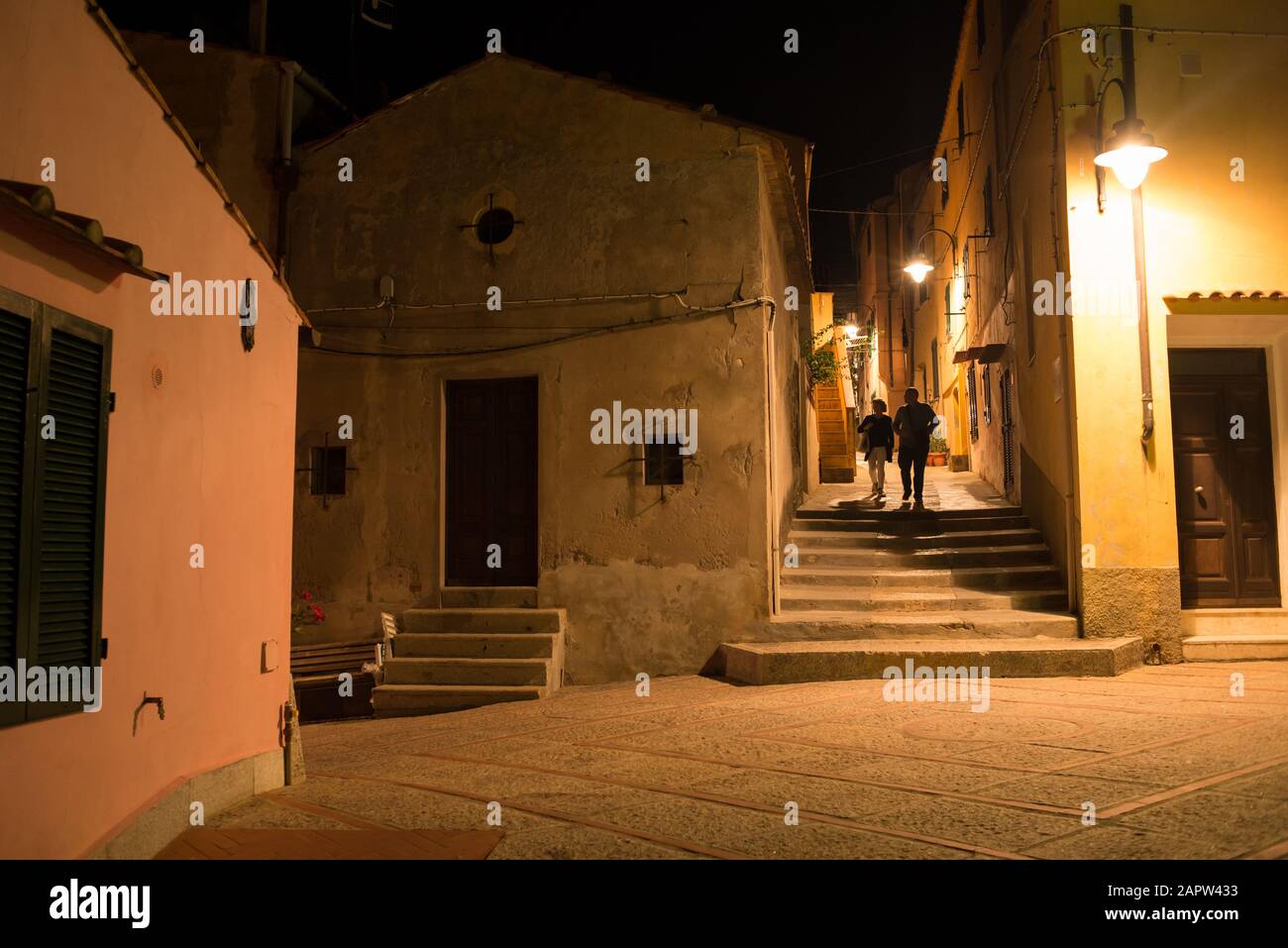 View of classic small alley in historic medieval Italian town at night with couple silhouettes walking Stock Photo