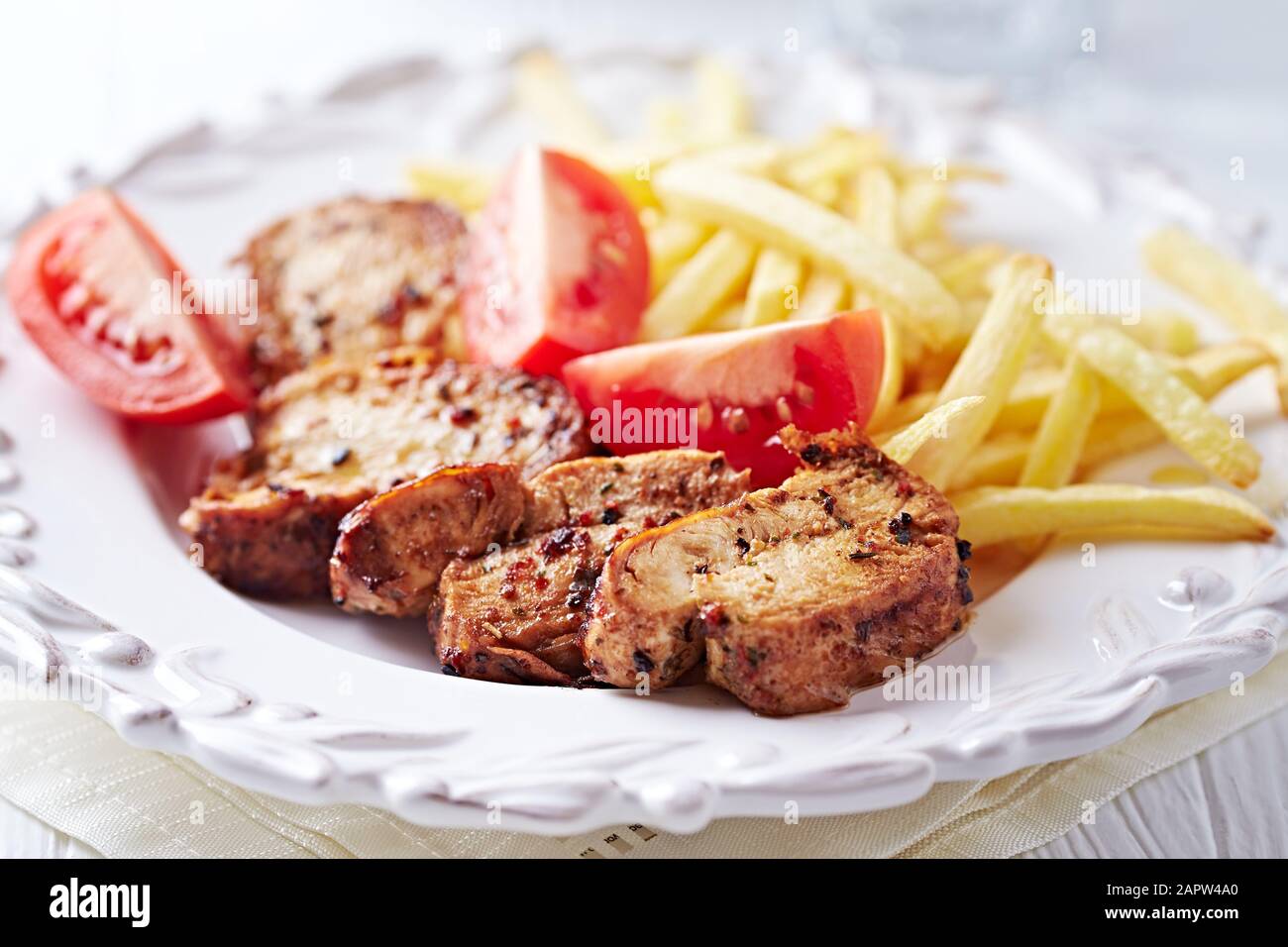 Fried pork tenderloin with tomatoas and french fries. Bright background