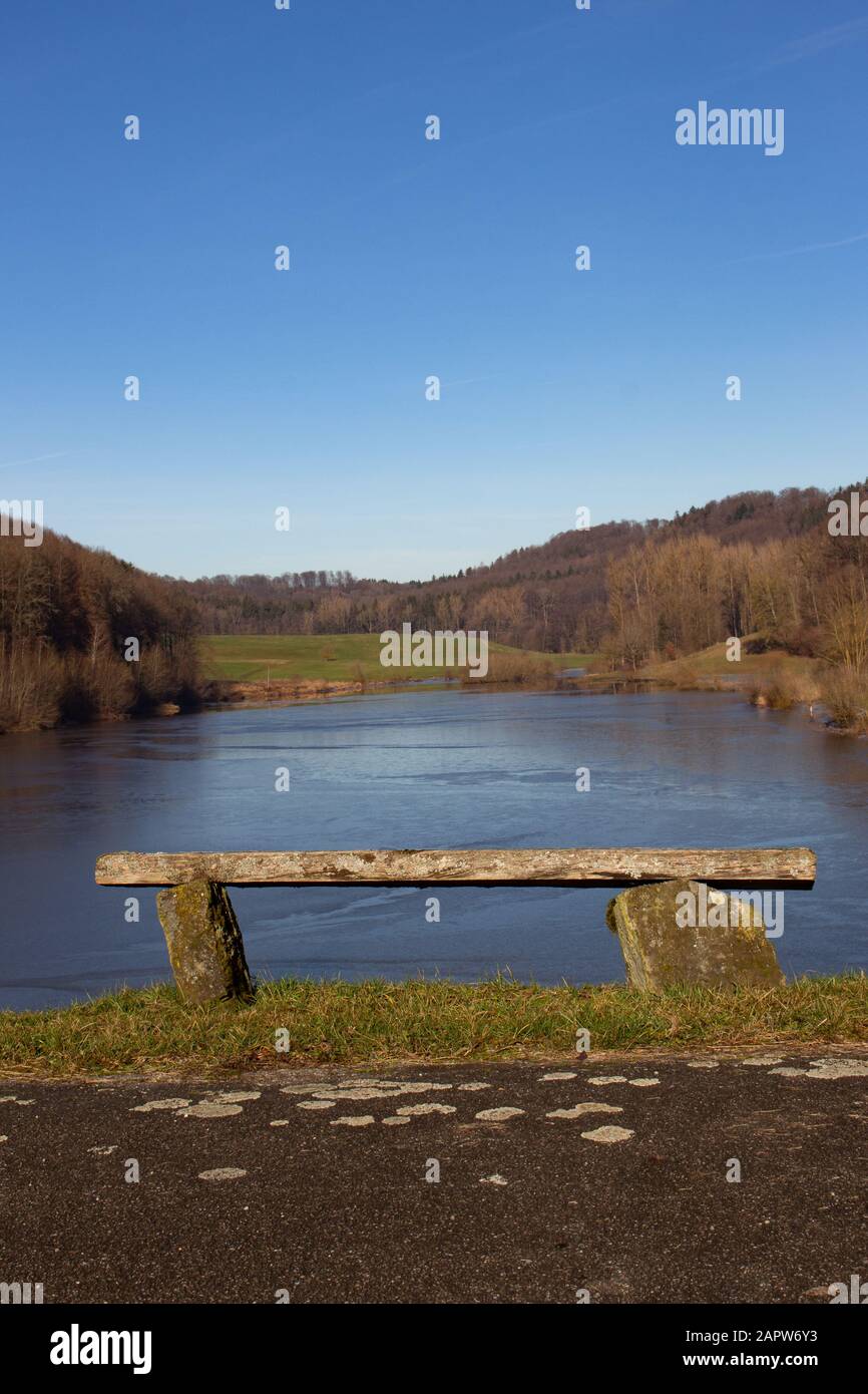 Tilted empty old wooden bench on a hill overlooking a frozen lake Stock Photo