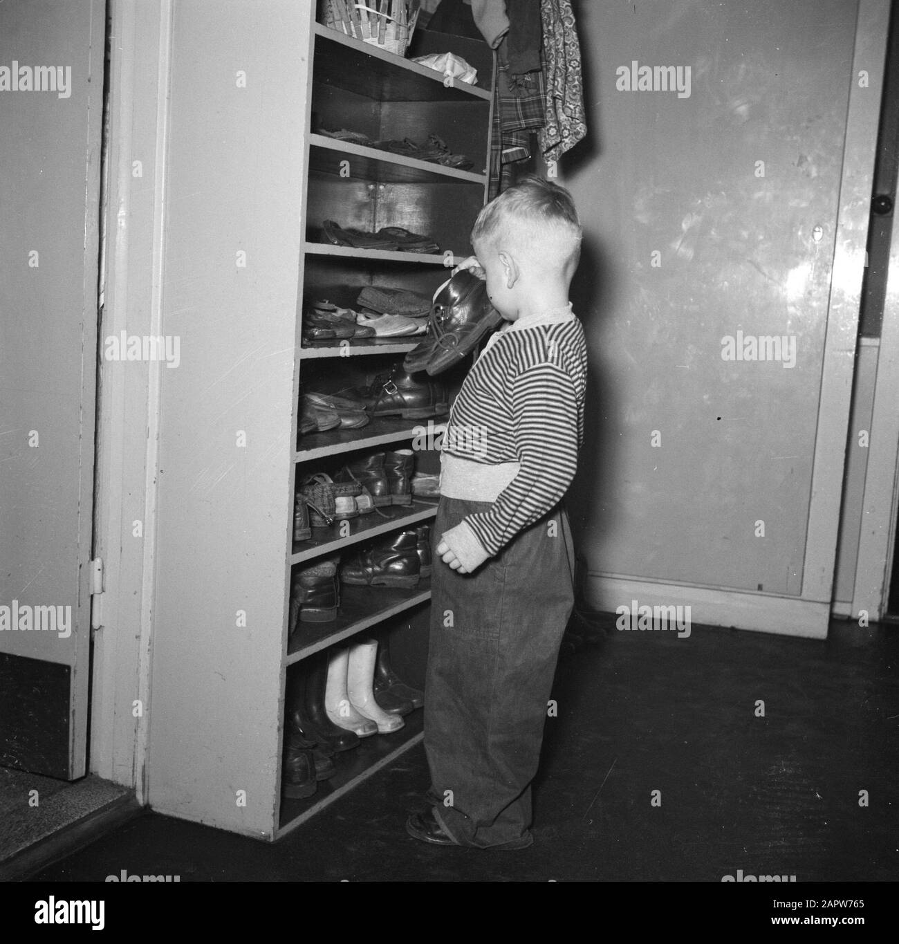 Look at the nursery of the Tuborg Brewery Preschooler with a pair of shoes  in hand near a closet full of shoes Date: March 1954 Location: Denmark,  Hellerup Keywords: childcare, etc. preschool