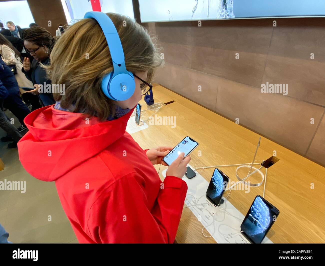 Paris, France - Nov 02, 2019: Side view woman in red coat inside Apple Computers Store testing listening to music with new latest Beats by Dr Dre Solo Pro Active Noise Cancelling headphones Stock Photo