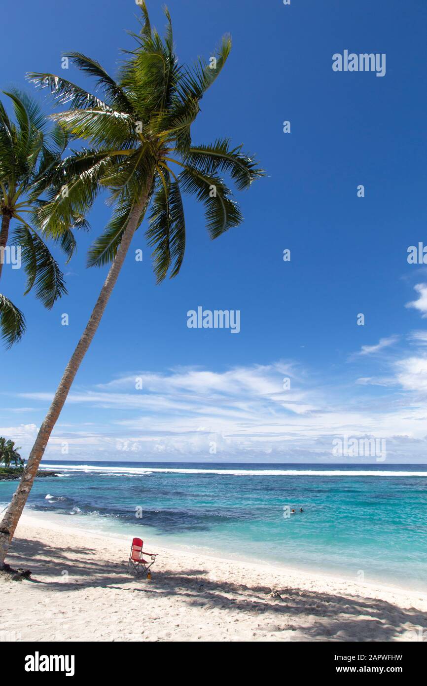 Red beach chair, under coconut palm tree at white sandy beach, Samoa Stock Photo