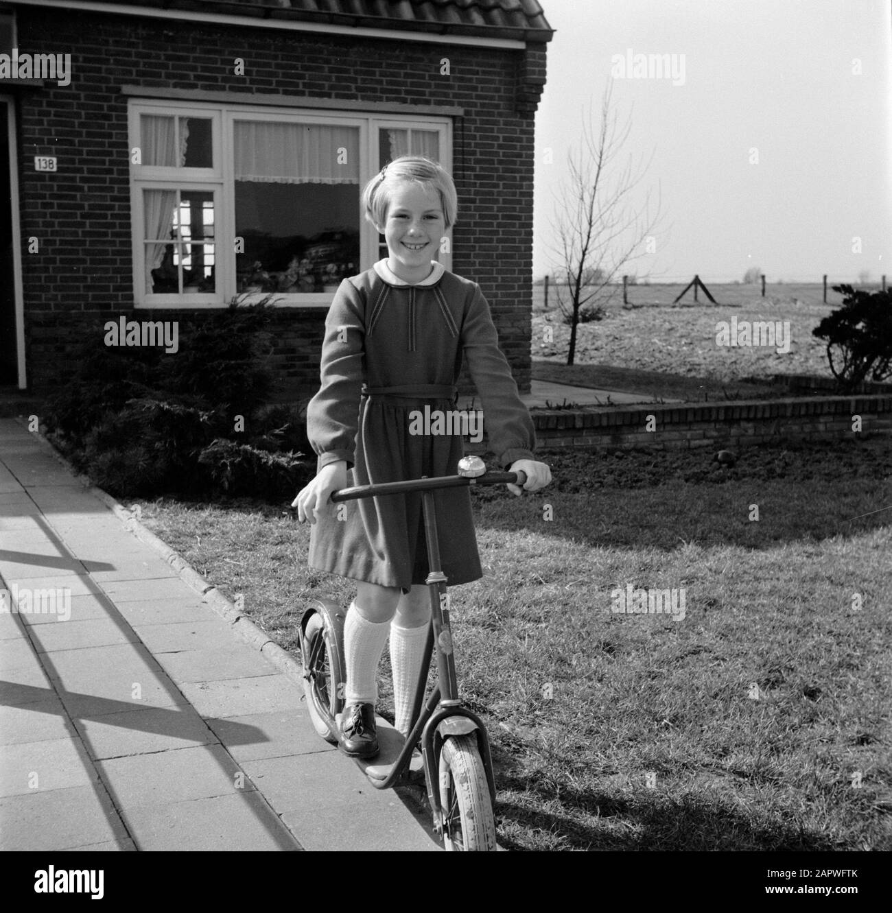 Marietje, the eight-year-old daughter of Gerard, on her autoped in the front garden Annotation: Gerard de Jong survived a fusillade on April 7, 1945 at Dronrijp Date: 1 January 1955 Location: Friesland, Leeuwarden Keywords: autopeds, girls, gardens, homes Personal name: Jong, Marietje de Stock Photo