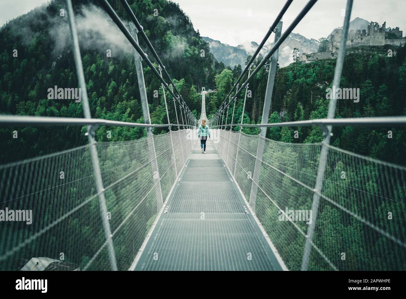 Young female hiking over suspension rope bridge in alpine environment Stock Photo