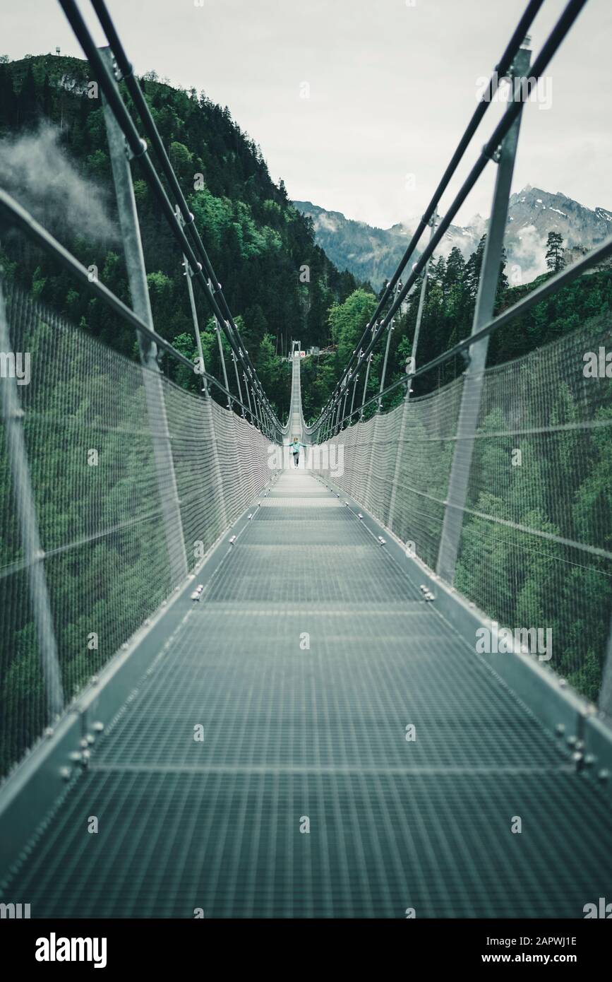 Young female crossing suspension rope bridge in alpine environment Stock Photo