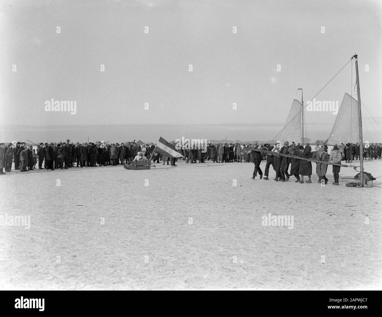 Ice spret on the frozen waters in the Netherlands  People stand in a large circle watching a so-called millet sleigh drawn on the ice of the Gouwzee Annotation: On a thick pole that passes through the ice was beaten long ropes were fastened. To these ropes, sleds were fastened. A cross timber was attached to the thick pole which was pushed by men with sharp under their clogs Date: 1931 Location: Gouwzee, Marken, Noord-Holland Keywords: ice, public, sleds, snow, winter Stock Photo