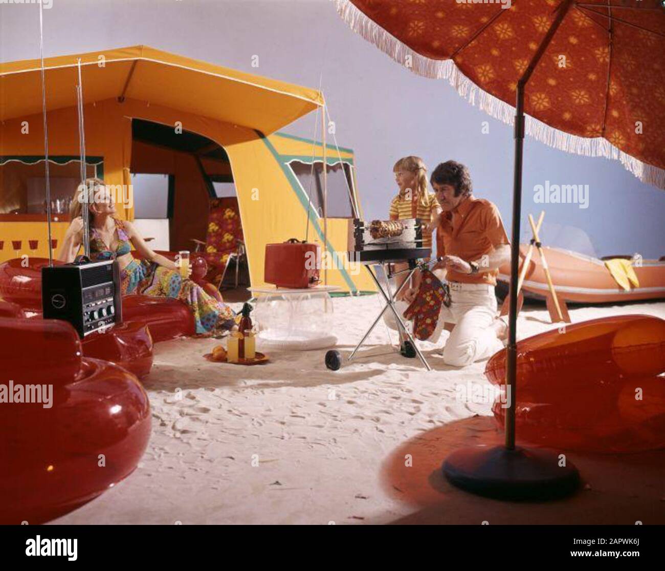 Studio recording of a camping modern family with a tent, red inflatable furniture, a parasol, a huge transistor radio, a barbecue, a portable television and an inflatable boat, 1967. Stock Photo