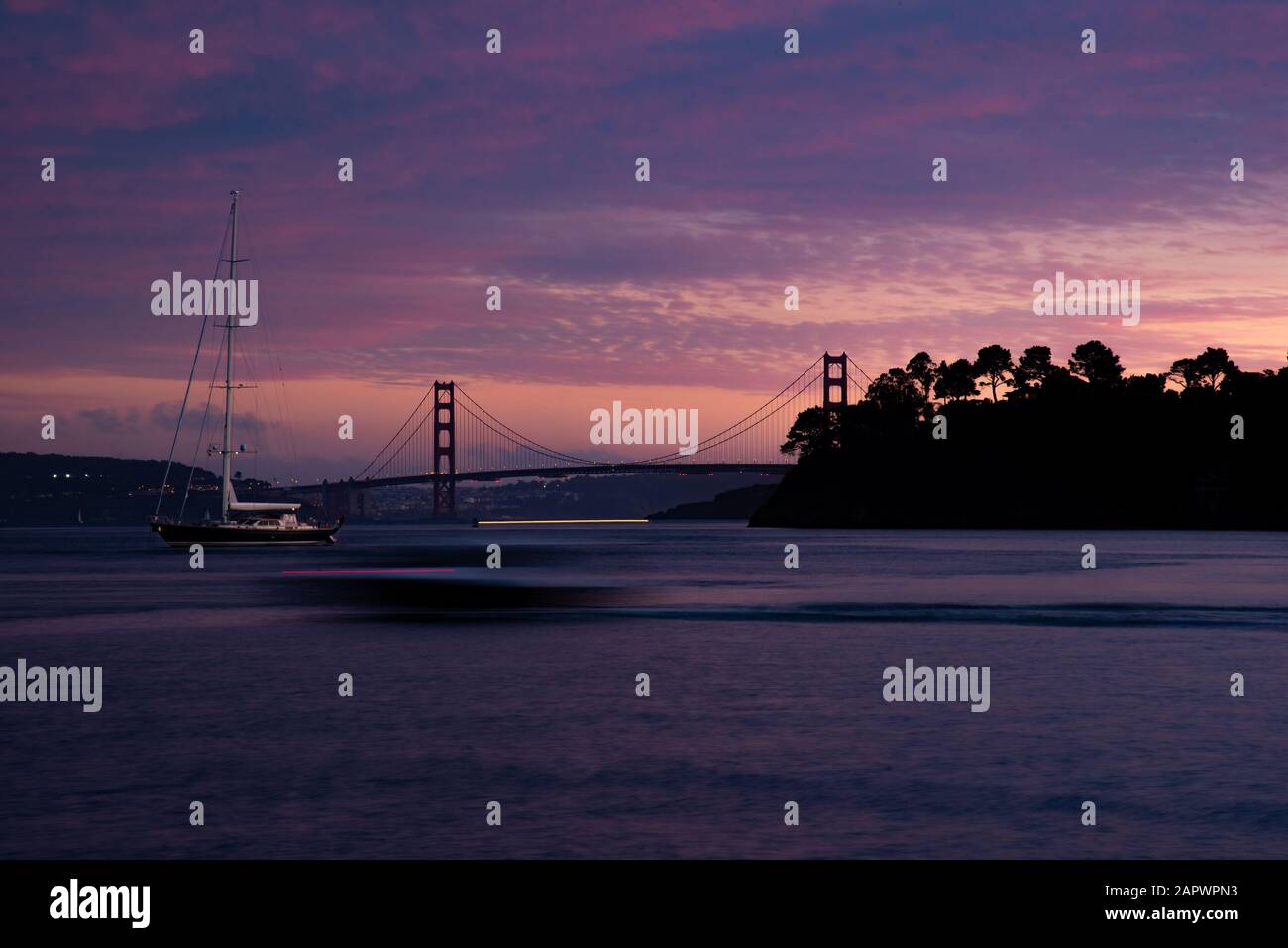 Shot of a Golden Gate Bridge Tiburon USA in the purple sky with a boat floating in the water Stock Photo