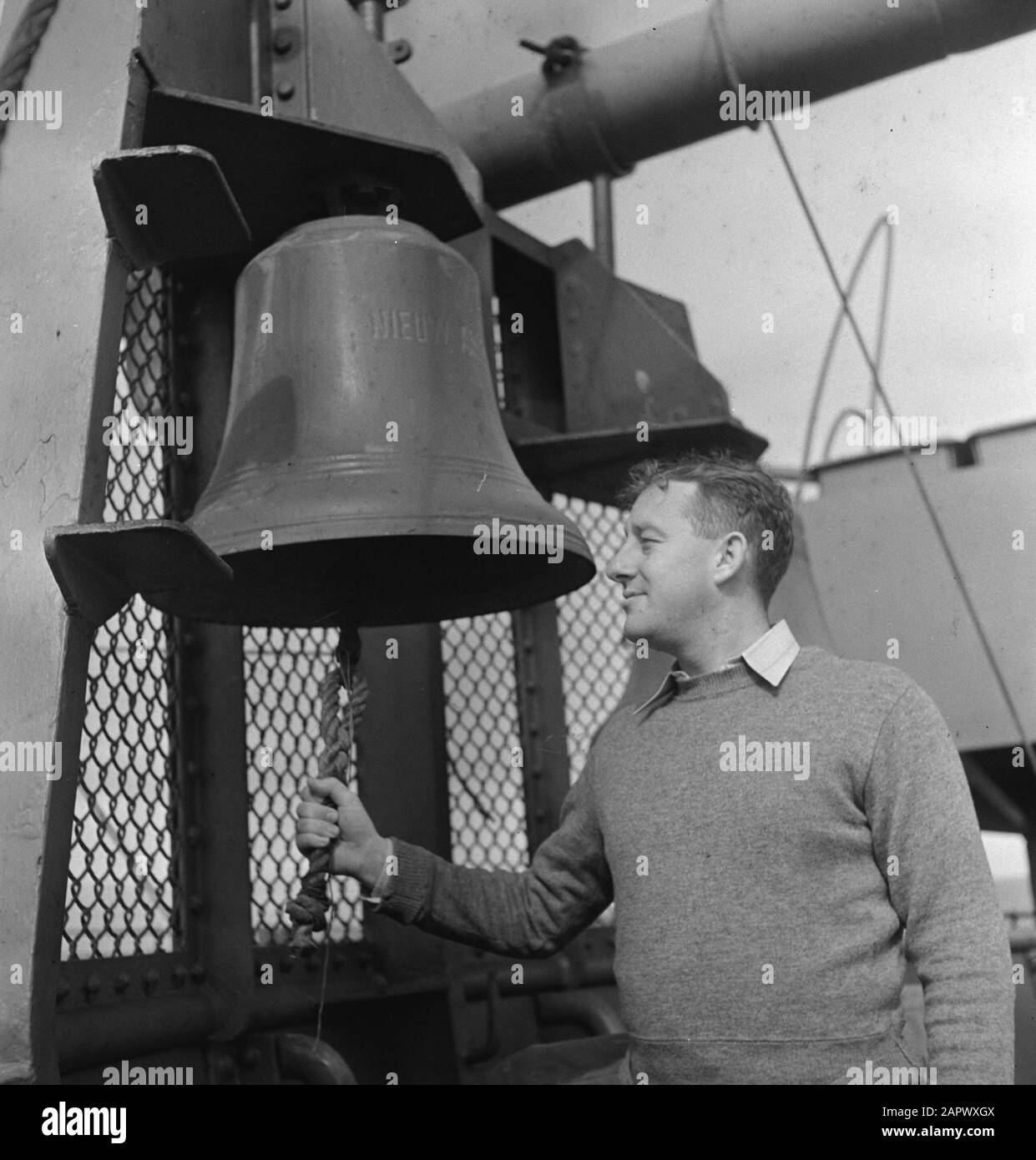 MN [Merchant Navy]/Anefo London series  On a Dutch passenger ship in service for troop transport. Man by ship bell (with inscription New...] Date: May 1944 Location: Canada Keywords: crew, merchant fleets, navy, passenger ships, ships, World War II Stock Photo