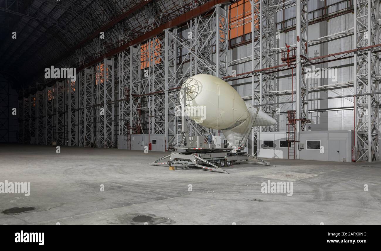 Small blimp on a mooring platform inside empty big airship hangar Stock Photo