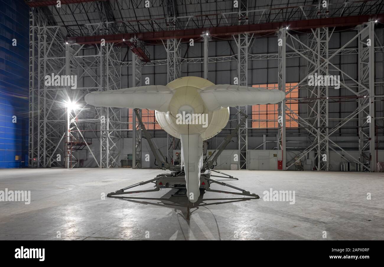 Small blimp on a mooring platform in a giant aircraft hangar. View from the back Stock Photo