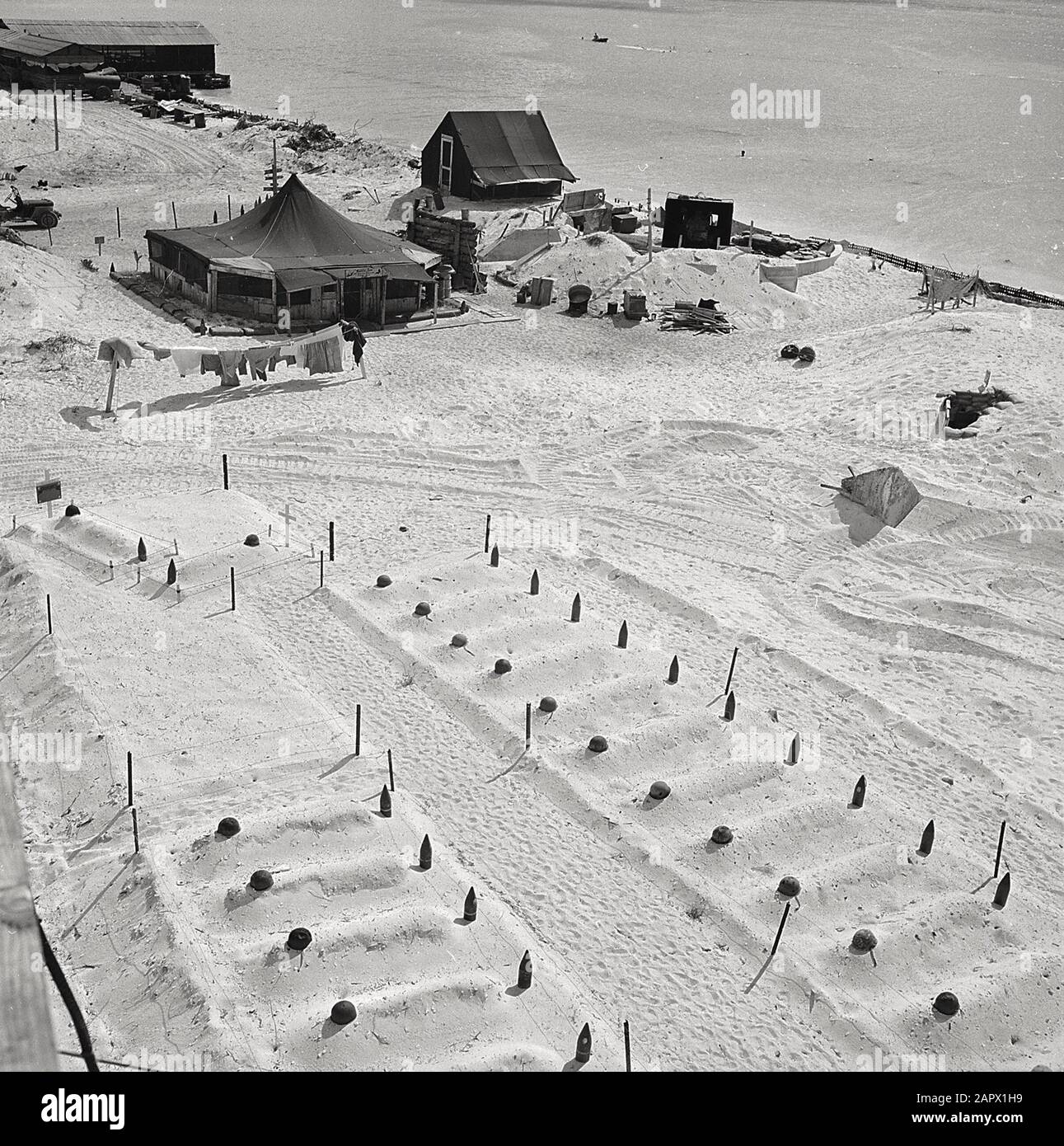 Empty helmets and spent artillery shells mark the graves of Marines who fell at Tarawa, March 1944. Graves of U.S. Marines who died taking Tarawa, before headstones were prepared. In the background are the first tents put up after occupation of the island. Stock Photo