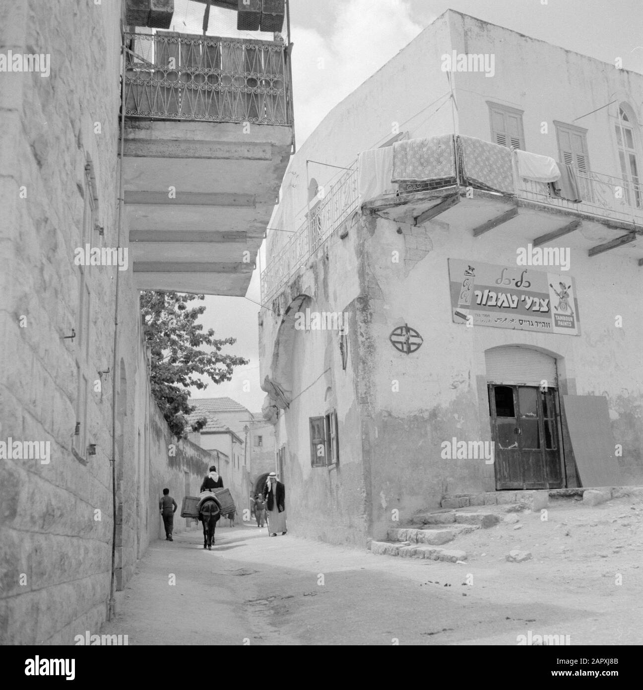 Israel: Nazareth  Street with a paint shop, pedestrian and a man riding a donkey Date: undated Location: Galilee, Israel, Nazareth Keywords: donkeys, street statues, pedestrians, shops Stock Photo