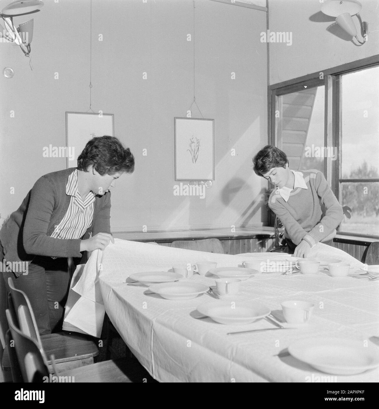 Israel 1964-1965: Gal'ed, since evening  Two people lay the finishing touches on decking tables for the celebration of Seideravond (sedermeal) Annotation: Gal'ed (also called Even Yitzhak) is a kibbutz in northern Israel, located in the plain of Manasseh. In 2006 it had a population of 405. Seder Evening (also called Seideravond) is an evening at the beginning of the Passover festival, where Jews from the Haggada read (booklet about the story of Jewish slavery in Egypt and the exodus from Egypt), drink 4 glasses of wine (or grape juice) and a festive sedermeal. Seder literally means order or o Stock Photo