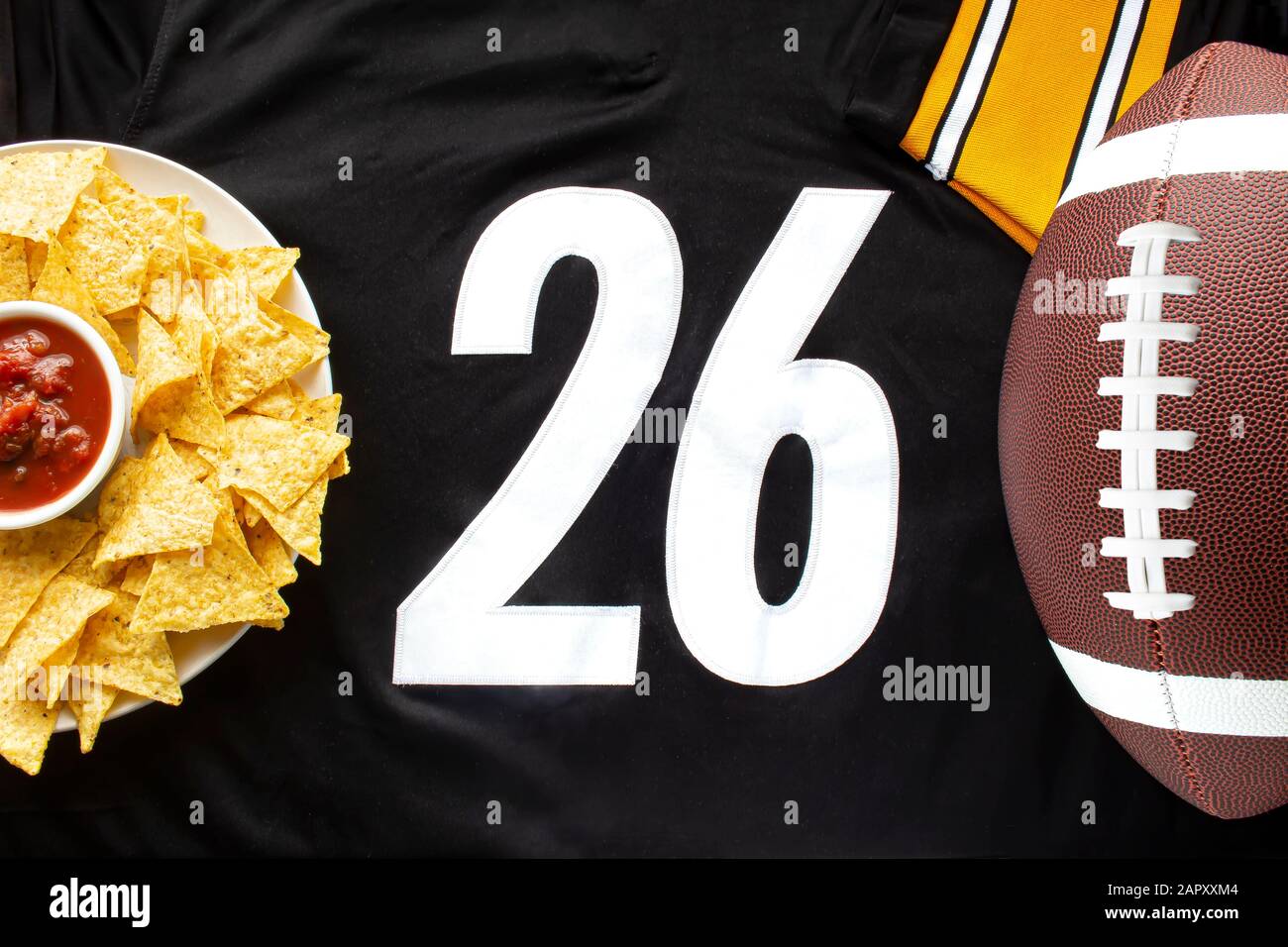 An American football with organic nacho chips and mild salsa on a white black football jersey with the 26 number on horizontal view Stock Photo