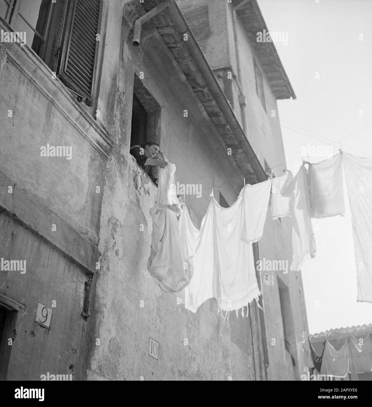 Rome: Visit to the city  Woman hangs laundry from a window on a line between houses above a small street in Trastevere Date: December 1937 Location: Italy, Rome Keywords: buildings, cityscape, street images, women, laundry, homes Stock Photo