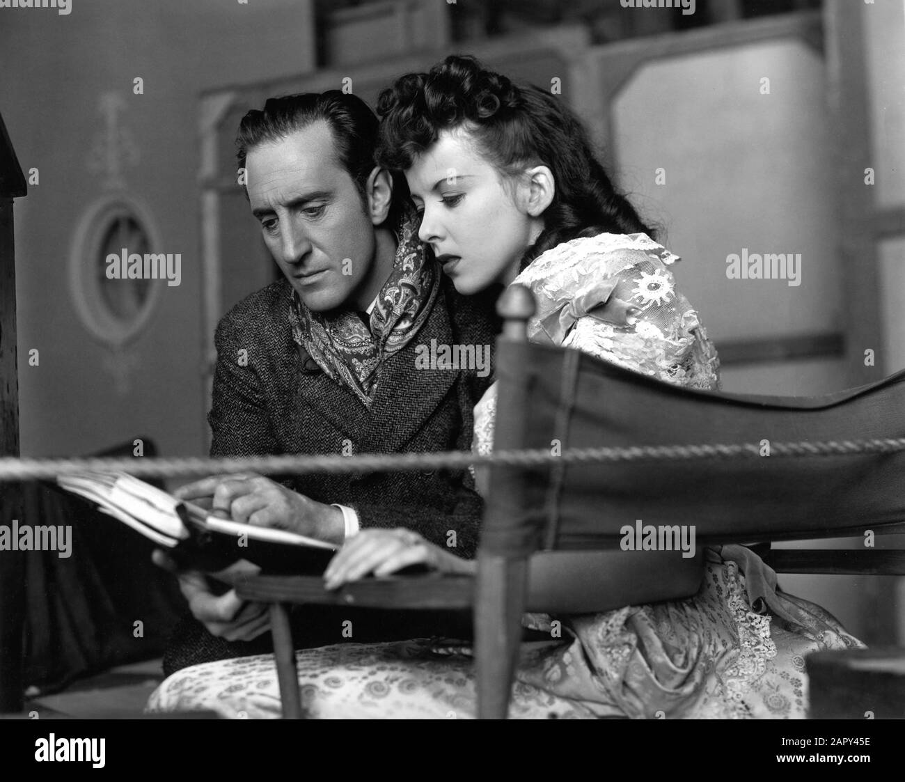 BASIL RATHBONE as Sherlock Holmes and IDA LUPINO on set candid during filming of THE ADVENTURES OF SHERLOCK HOLMES 1939 director ALFRED L. WERKER characters created by ARTHUR CONAN DOYLE Twentieth Century Fox Stock Photo