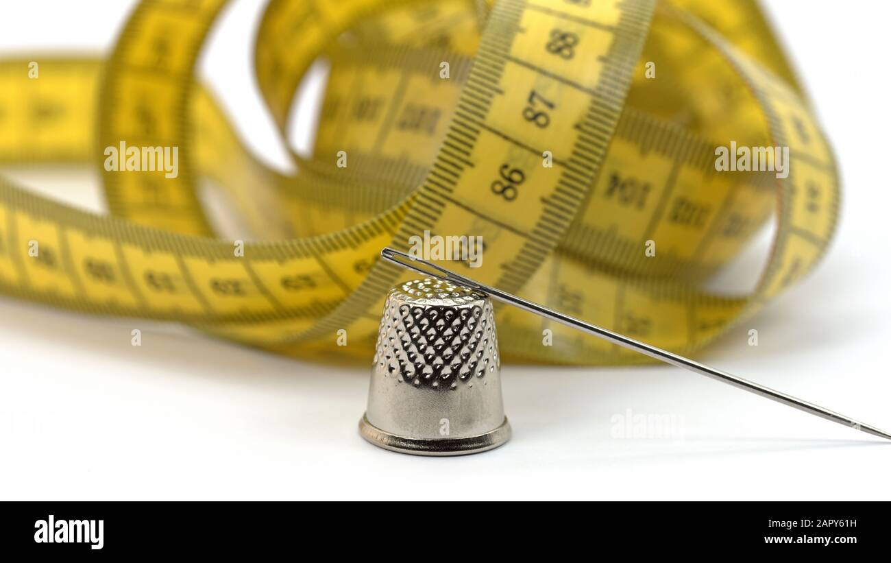 Tape measure, sewing needle and thimble against white background