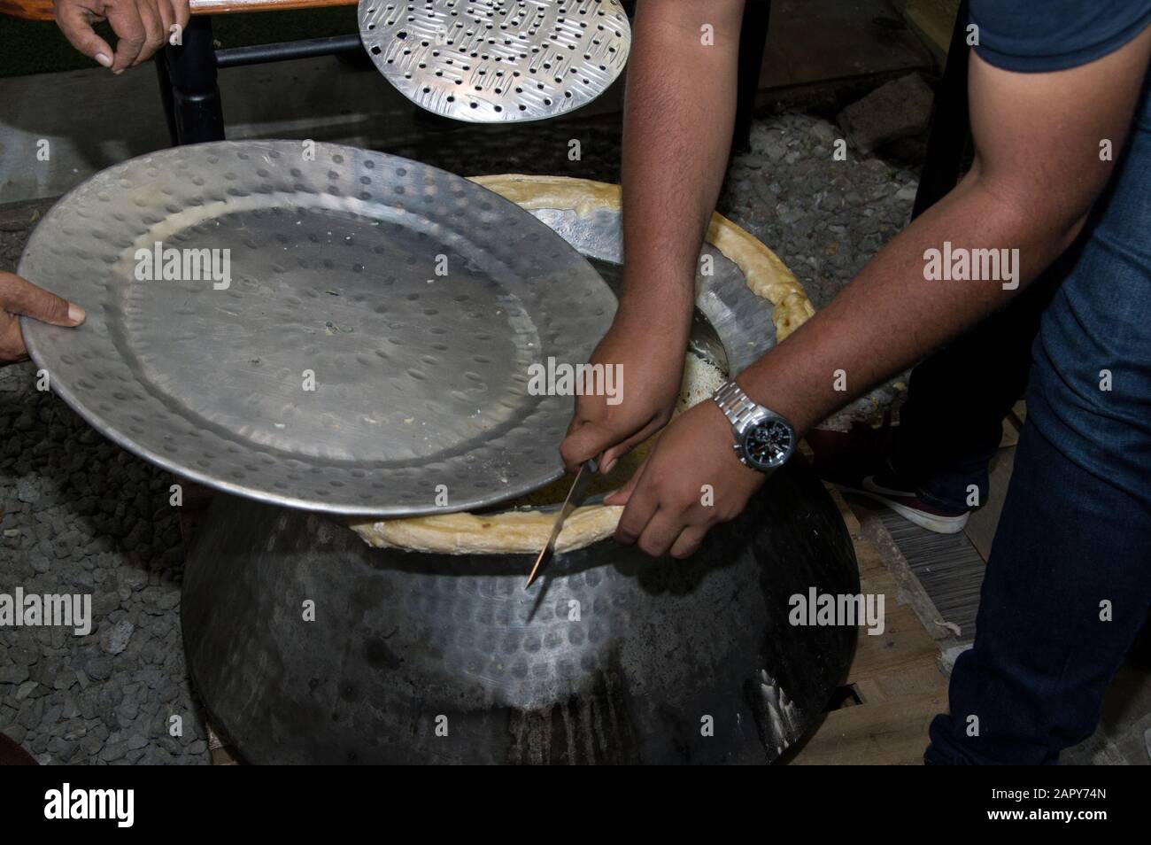 Chef's hands cut bread around an aluminum biriyani pot