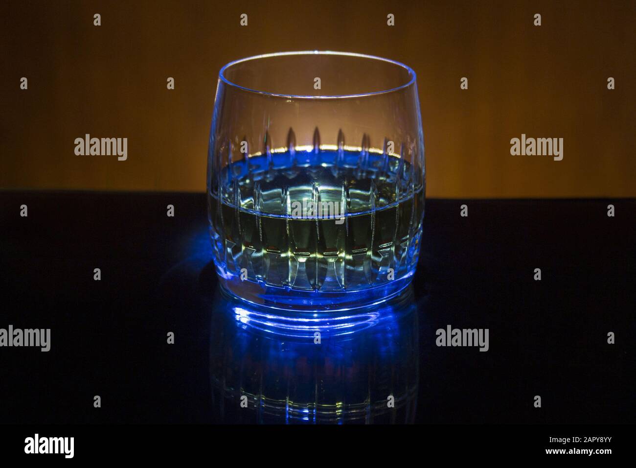 Glass with whiskey on gold background in blue light Stock Photo