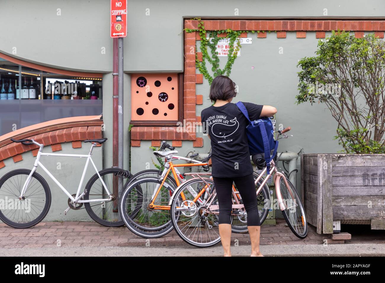 Byron Bay asian lady selects her bicycle from amongst those parked together In a side street,Australia Stock Photo