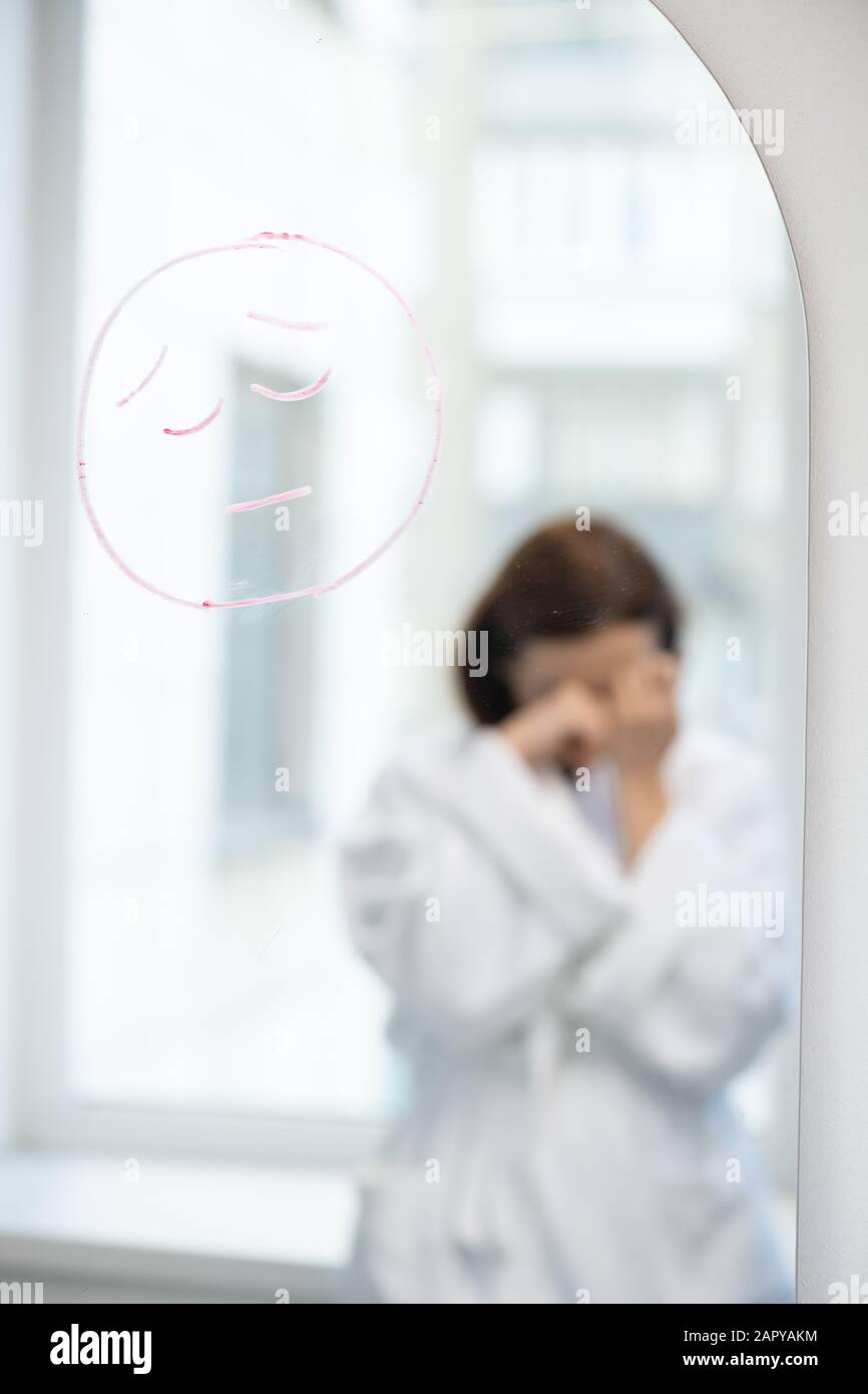 Upset face drawn with lipstick on mirror and reflection of unhappy ...