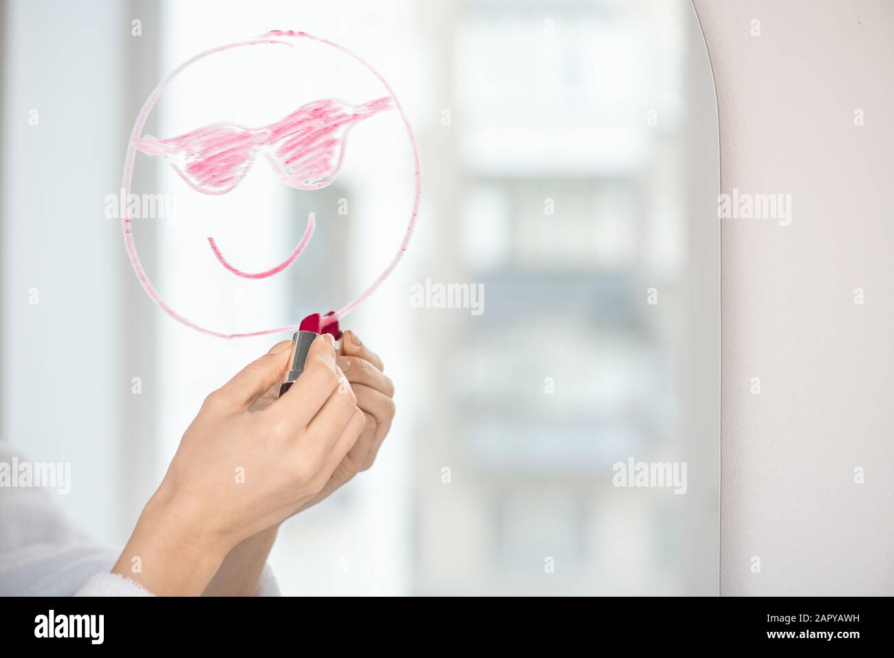 Hand of girl with lipstick drawing face with smile and sunglasses on mirror Stock Photo
