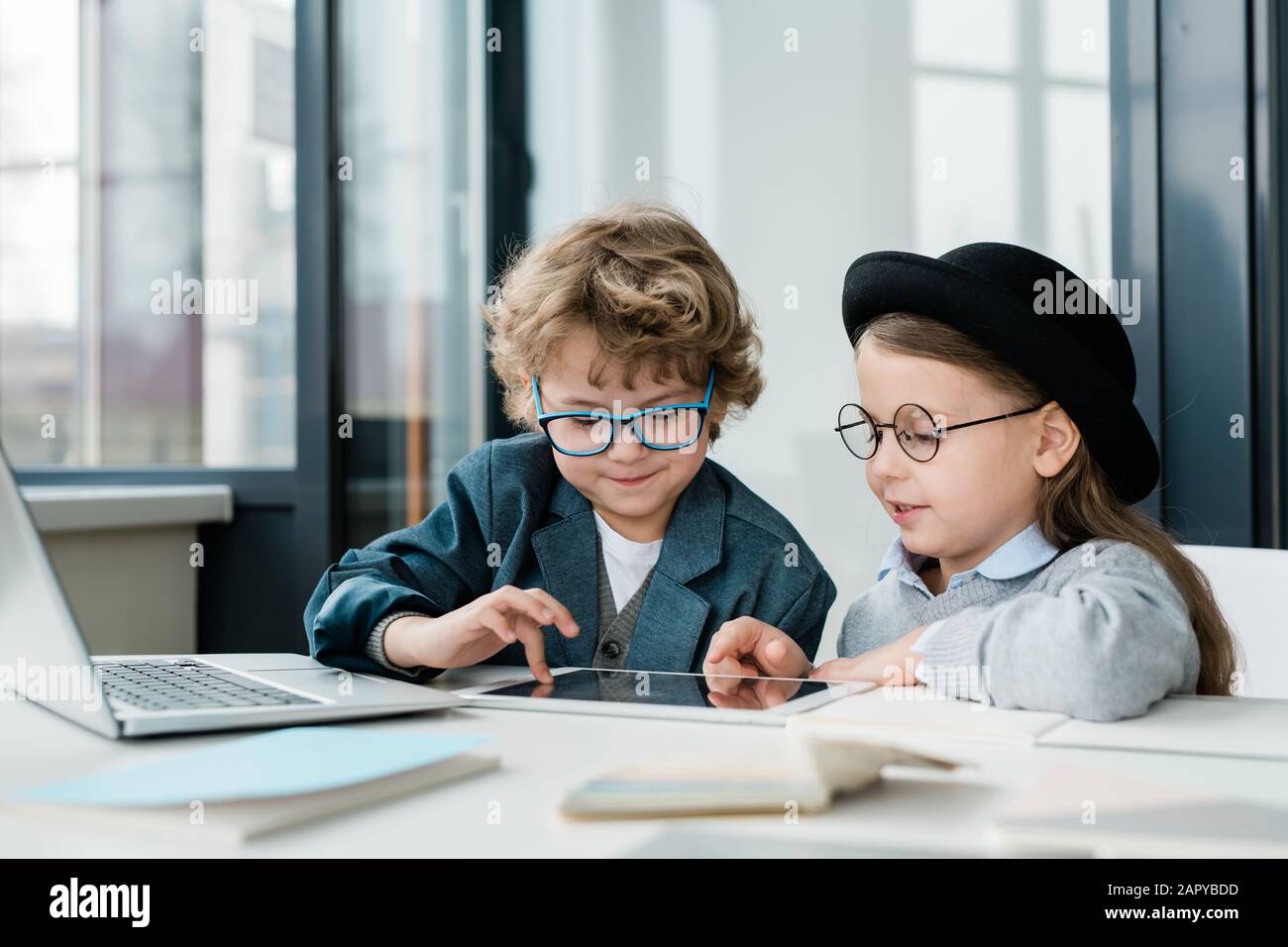 Cute elementary school friends in casualwear and eyeglasses using digital tablet Stock Photo