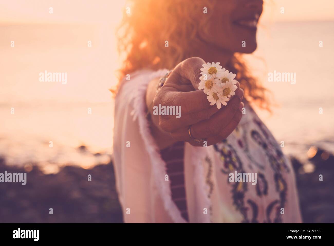 Environment and love for nature concept with cheerful happy woman in background holding some beautiful daisies with the hand - sun in backlight - suns Stock Photo
