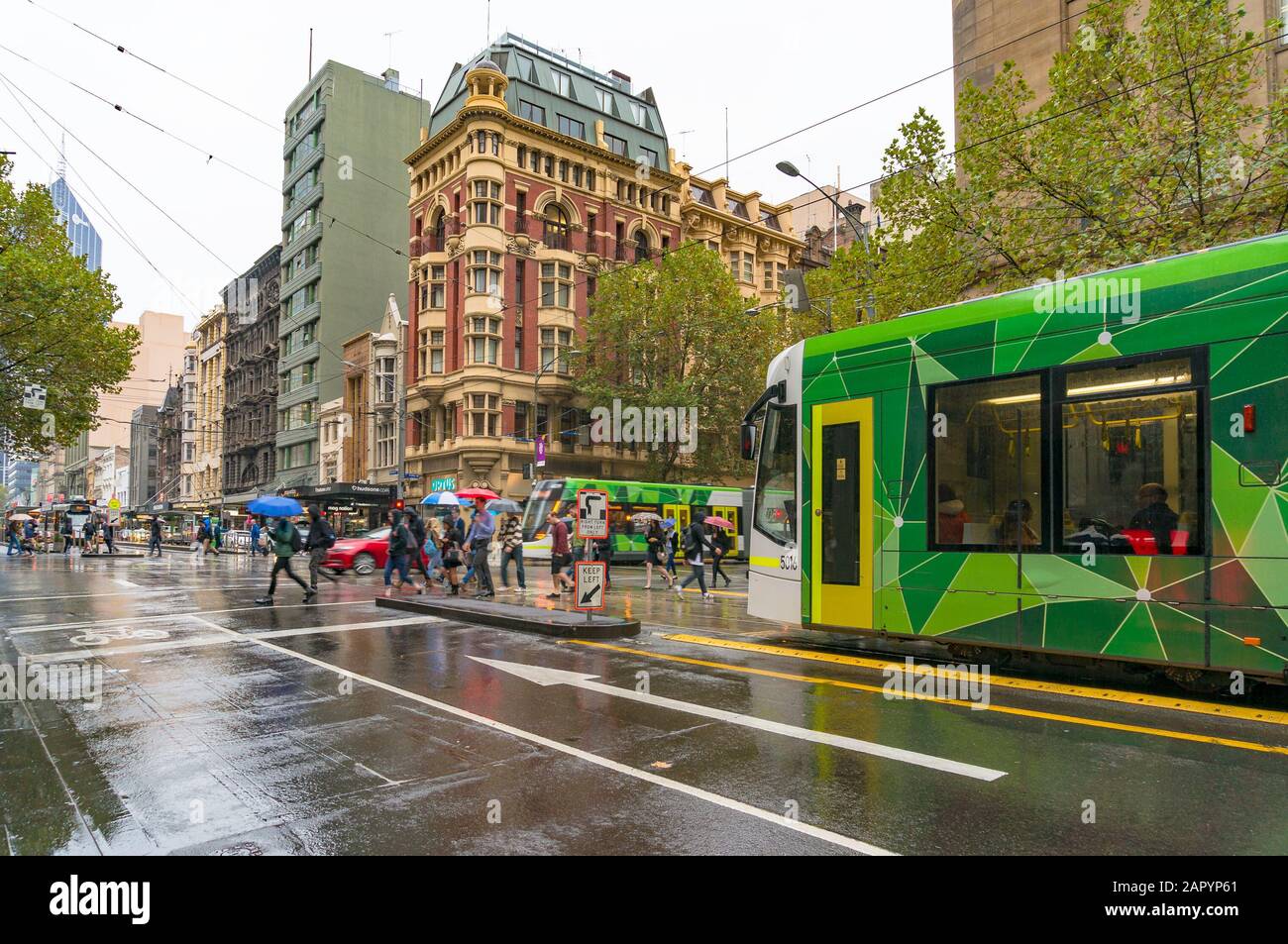 Melbourne, Australia - April 21, 2017: Melbourne urban infrastructure. People crossing intersection and tram stopping on red lights on rainy weather Stock Photo