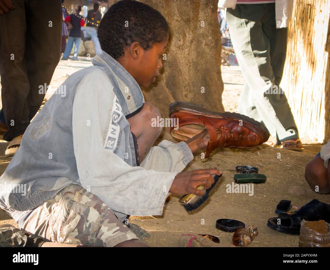 Young shoe cleaner cleaning and polishing leather shoes sitting on