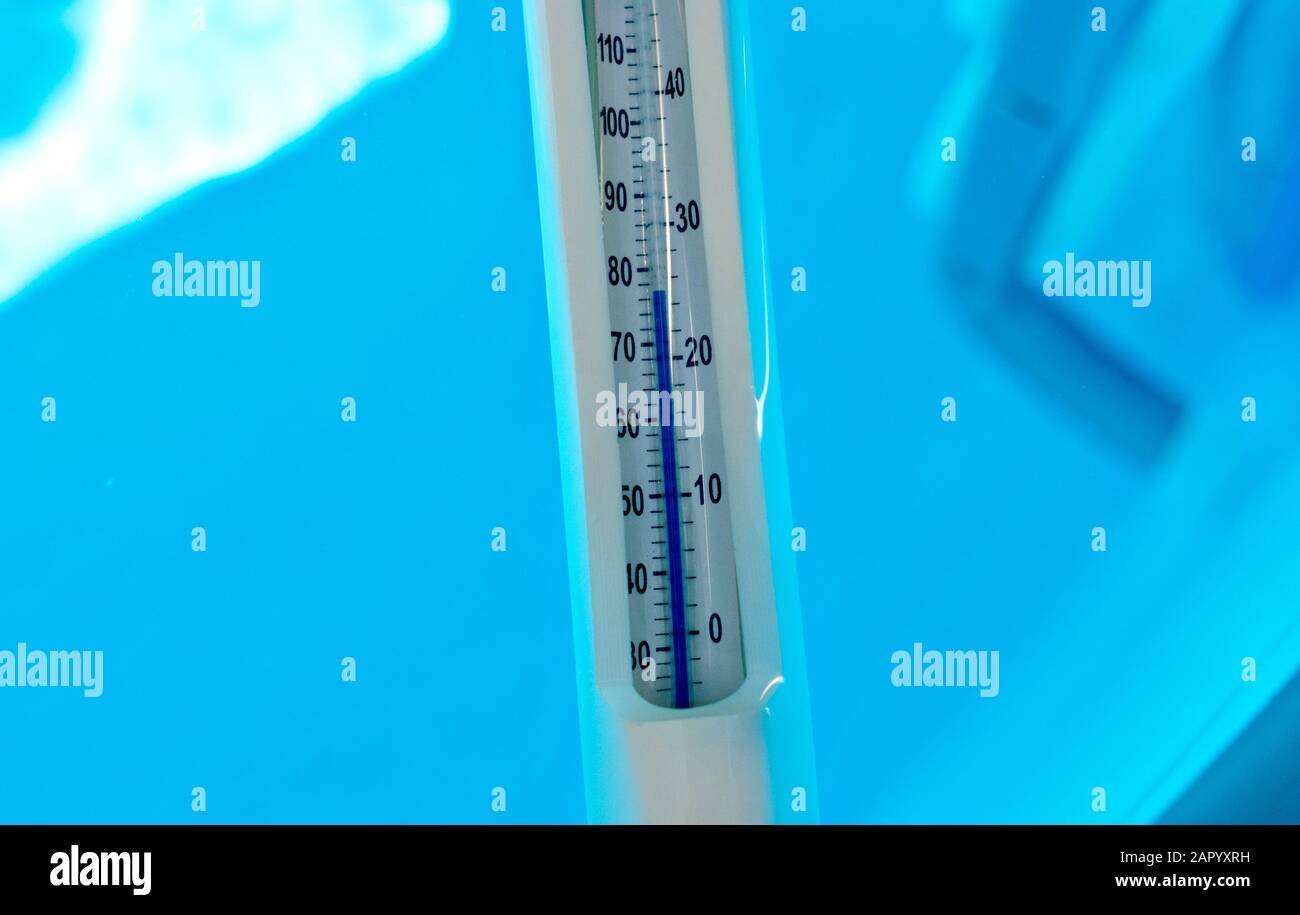 white pool thermometer displaying a temperature of 25 degrees Celsius oder 77 degrees Fahrenheit befor blue pool water Stock Photo